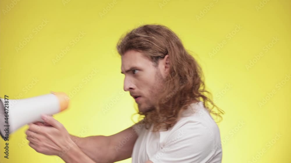 Cheerful funny young man in casual white t-shirt have fun isolated on yellow background studio. People sincere emotions lifestyle concept. Male screaming and play with megaphone. Slow motion. Cheerful funny young man in casual white t-shirt have fun isolated on yellow background studio. People sincere emotions lifestyle concept. Male screaming and play with megaphone. Slow motion.