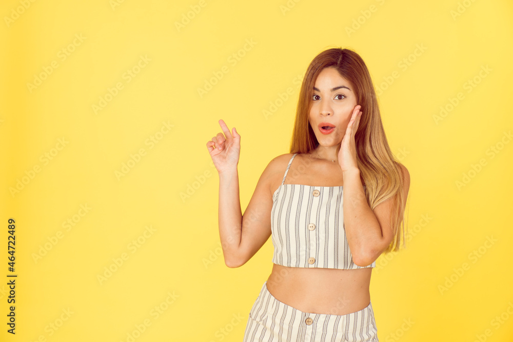 Young latin woman pointing to text, smile and surprise on yellow background. Young latin woman pointing to text, smile and surprise on yellow background.