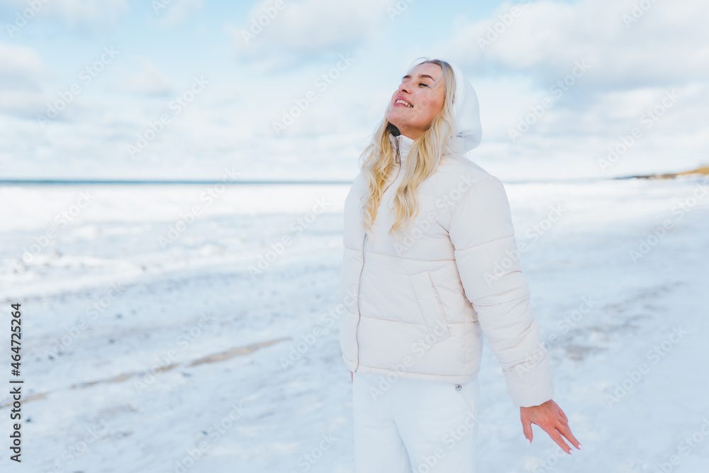 Woman wearing white clothes feels the cold on winter coast. Female breathe with cold fresh air