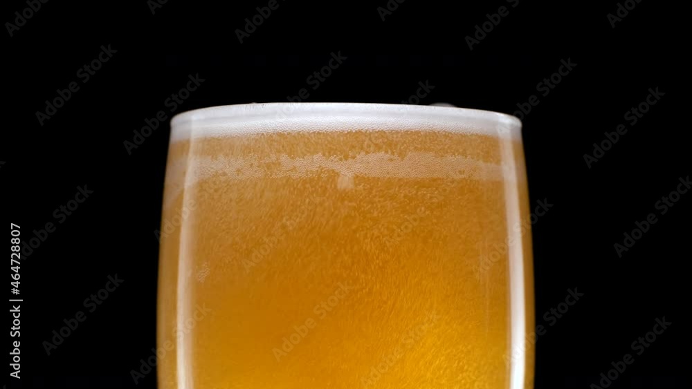 Light beer is pouring into glass. Cold lager beer in a beer mug on a black background with water droplets and foam. Isolated black background Light beer is pouring into glass. Cold lager beer in a beer mug on a black background with water droplets and foam. Isolated black background
