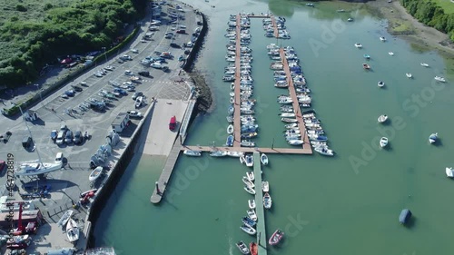 small boats moored at the jetty of Batson creek in Salcombe, a popular resort town, South Hams district of Devon. At the boat ramp there is a red car. Drone aerial birds eye view shot photo