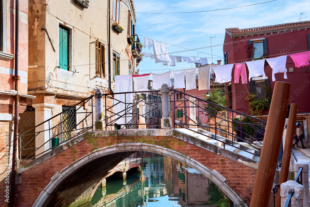 Washing lines across canal in Venice, Italy. Laundry hanging on a clothes line between city buildings and above bridge. Clothes lines between windows of old brick houses in Venice.