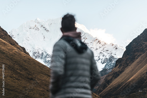 Man blurred out of focus looking up at snow capped mountain peaks