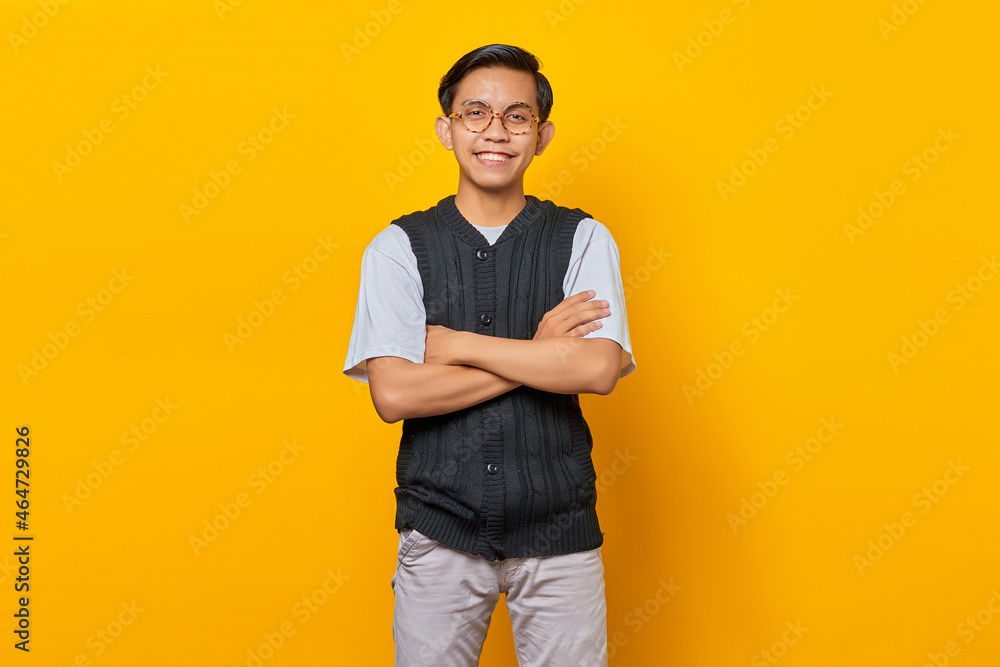 Portrait of smiling young Asian man looking at camera with crossed arms isolated on yellow background Portrait of smiling young Asian man looking at camera with crossed arms isolated on yellow background