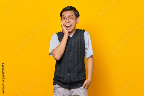 Portrait of surprised young Asian man looking at camera isolated on yellow background