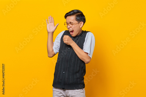 Happy young Asian man enjoying singing on yellow background