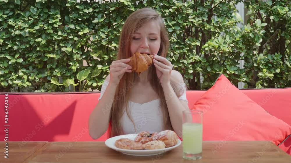 Pretty Girl Eat Croissant Sitting in Outdoor Cafe in Sunny Day. Plate Full of Fresh Food, Bakery, Pastry, Buns, Glass of Green Fruit Juice on Wooden Table. Concept of Sweet Morning Breakfast in Hotel. Pretty Girl Eat Croissant Sitting in Outdoor Cafe in Sunny Day. Plate Full of Fresh Food, Bakery, Pastry, Buns, Glass of Green Fruit Juice on Wooden Table. Concept of Sweet Morning Breakfast in Hotel.