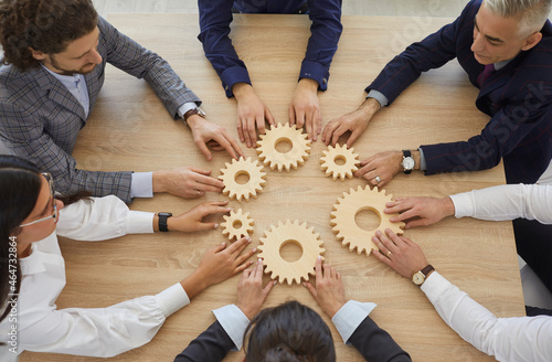 Team of businesspeople developing good business system. Group of senior and young business people sitting around table join gearwheels as metaphor for good effective teamwork. High angle, from above photo