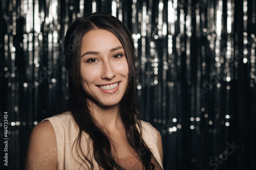 A young attractive woman smiles at a party, on a silver shiny background