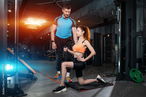 young woman exercising single arm row kneeling with personal trainer man in gym