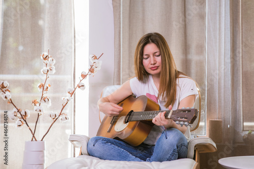 Young woman playing guitar at home. Learning play music instrument. Leisure time hobby.