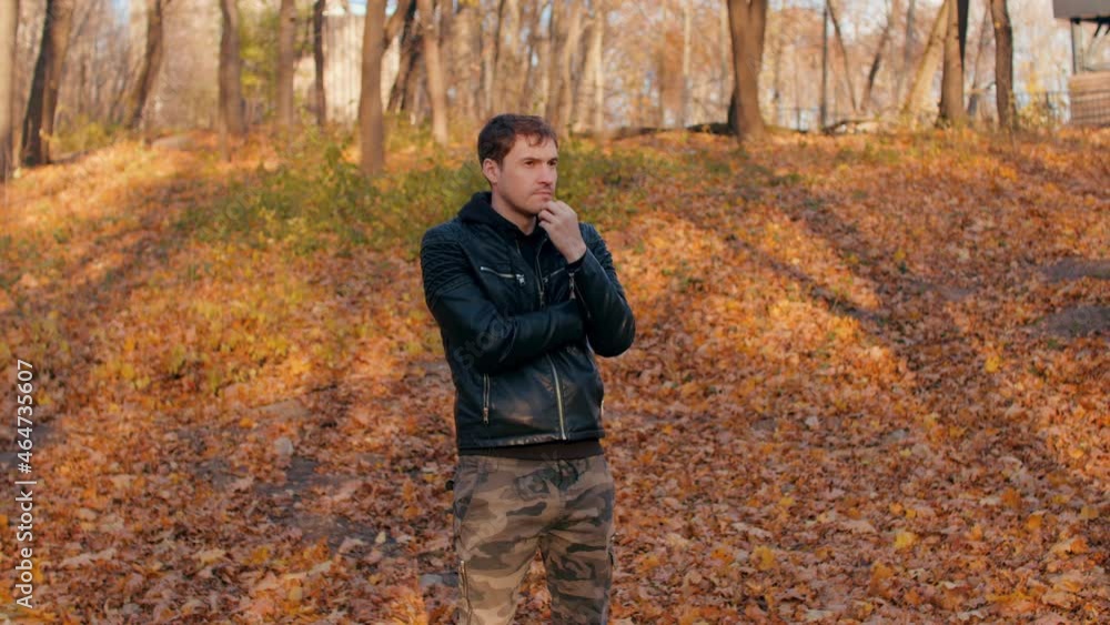 Young man in autumn forest. Thoughtful male scratches his chin while standing in city park. Young man in autumn forest. Thoughtful male scratches his chin while standing in city park.