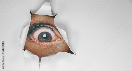 Eye peeking through peep hole watching something scary. Scared woman with look of horror in her eyes looking peeping from a dark room at night photo