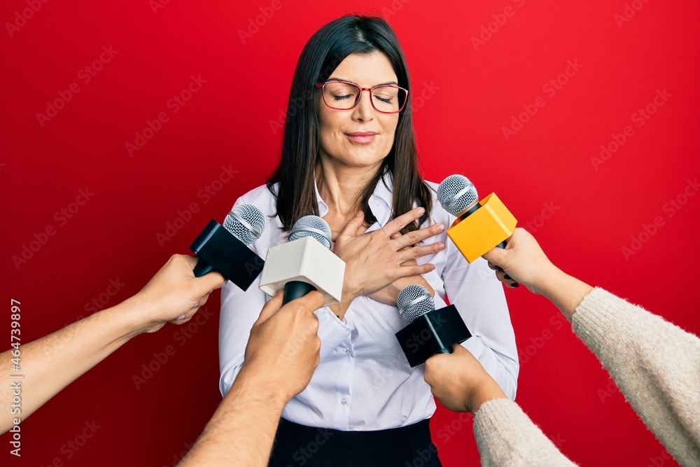 Young hispanic woman being interviewed for journalist hands with microphone smiling with hands on chest, eyes closed with grateful gesture on face. health concept. Young hispanic woman being interviewed for journalist hands with microphone smiling with hands on chest, eyes closed with grateful gesture on face. health concept.