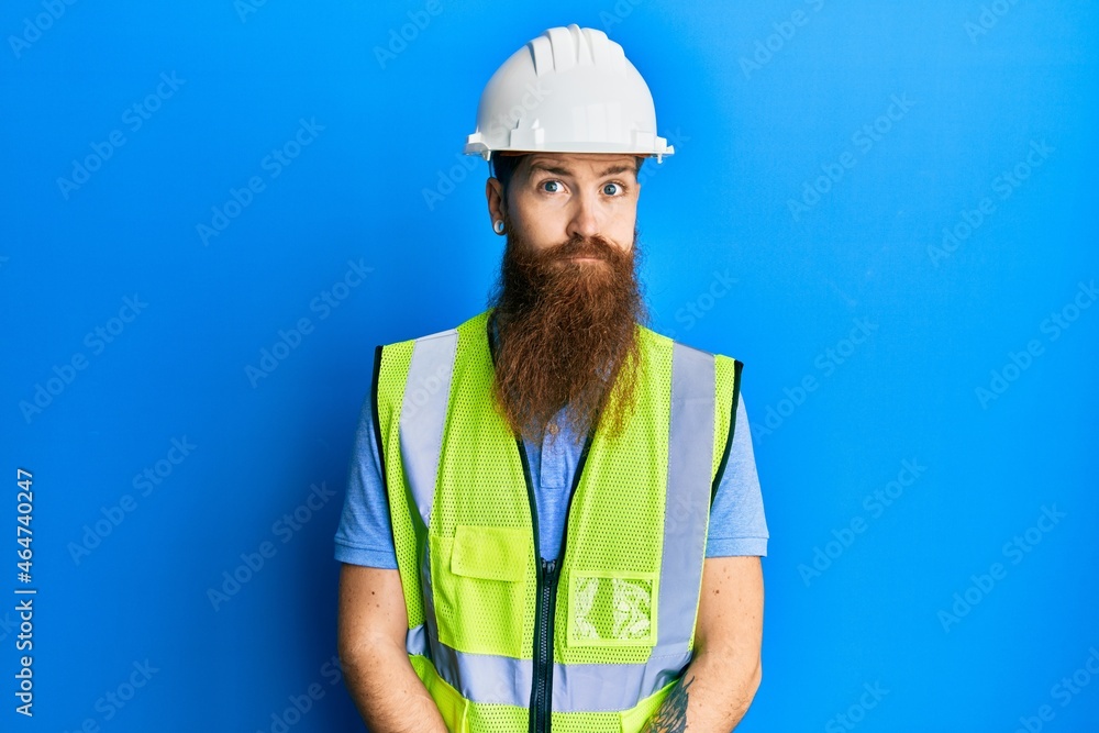 Redhead man with long beard wearing safety helmet and reflective jacket puffing cheeks with funny face. mouth inflated with air, crazy expression. Redhead man with long beard wearing safety helmet and reflective jacket puffing cheeks with funny face. mouth inflated with air, crazy expression.