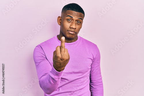 Young black man wearing casual pink sweater showing middle finger, impolite and rude fuck off expression