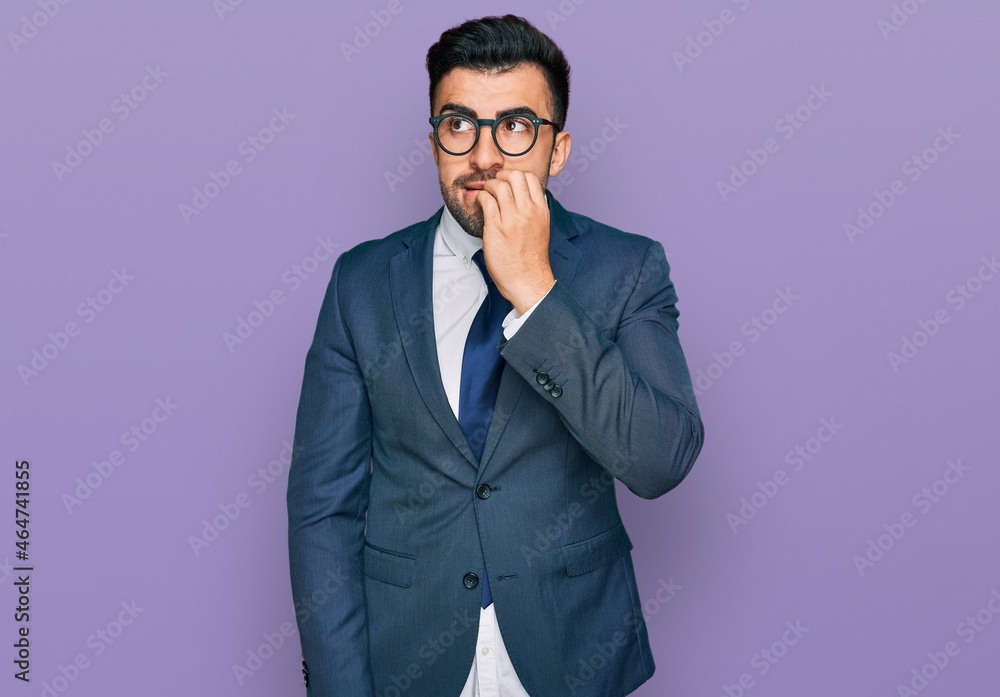 Hispanic man with beard wearing business suit and tie looking stressed and nervous with hands on mouth biting nails. anxiety problem. Hispanic man with beard wearing business suit and tie looking stressed and nervous with hands on mouth biting nails. anxiety problem.