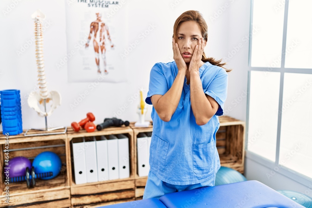 Middle age hispanic physiotherapist woman working at pain recovery clinic tired hands covering face, depression and sadness, upset and irritated for problem Middle age hispanic physiotherapist woman working at pain recovery clinic tired hands covering face, depression and sadness, upset and irritated for problem