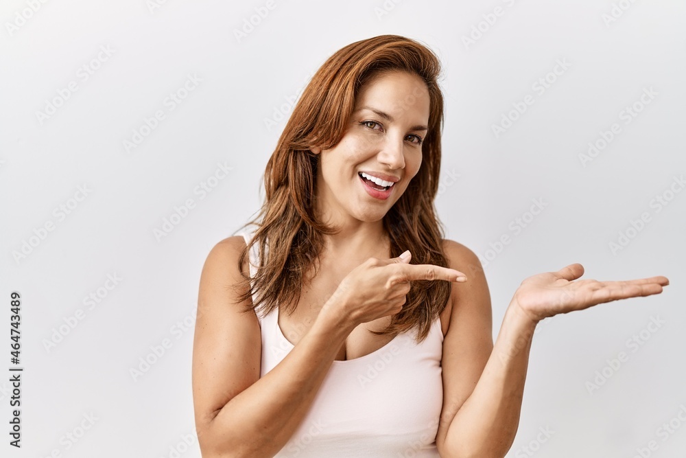 Middle age hispanic woman standing over isolated background amazed and smiling to the camera while presenting with hand and pointing with finger. Middle age hispanic woman standing over isolated background amazed and smiling to the camera while presenting with hand and pointing with finger.