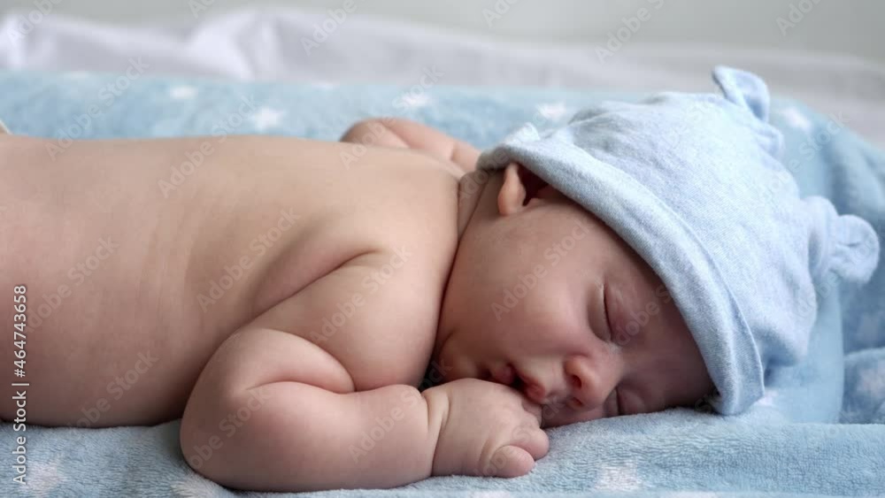 infancy, childhood, development, health, love, care concept - top view close-up face of newborn naked sleeping little small infant baby boy in hat lying on stomach on soft blue banket on bed at home infancy, childhood, development, health, love, care concept - top view close-up face of newborn naked sleeping little small infant baby boy in hat lying on stomach on soft blue banket on bed at home
