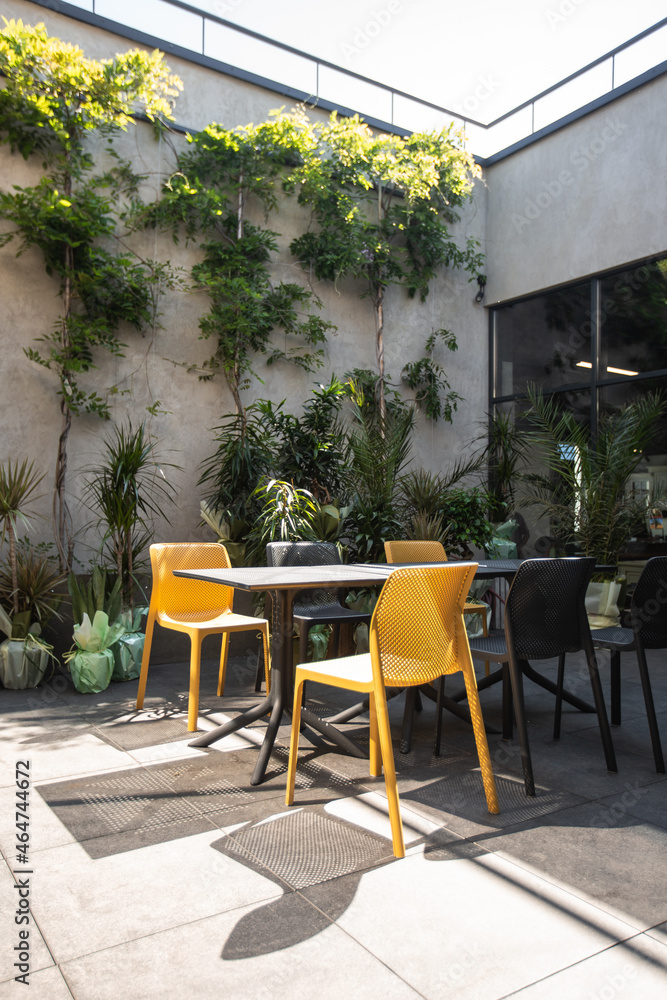 Bright garden furniture and plants on cozy terrace with wooden floor and brick wall. Interior of a summer terrace of a restaurant
