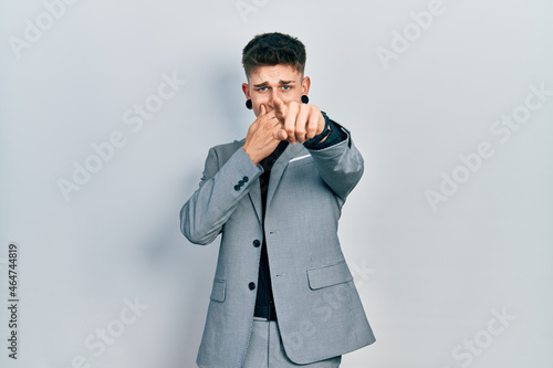 Young caucasian boy with ears dilation wearing business jacket laughing at you, pointing finger to the camera with hand over mouth, shame expression © Krakenimages.com