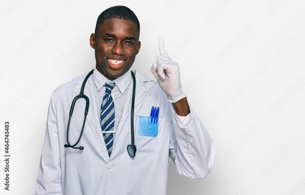 Young african american man wearing doctor uniform and stethoscope pointing finger up with successful idea. exited and happy. number one. Young african american man wearing doctor uniform and stethoscope pointing finger up with successful idea. exited and happy. number one.