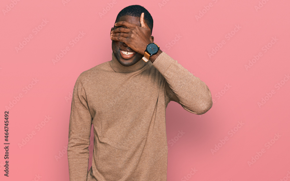 Young african american man wearing casual winter sweater smiling and laughing with hand on face covering eyes for surprise. blind concept. Young african american man wearing casual winter sweater smiling and laughing with hand on face covering eyes for surprise. blind concept.