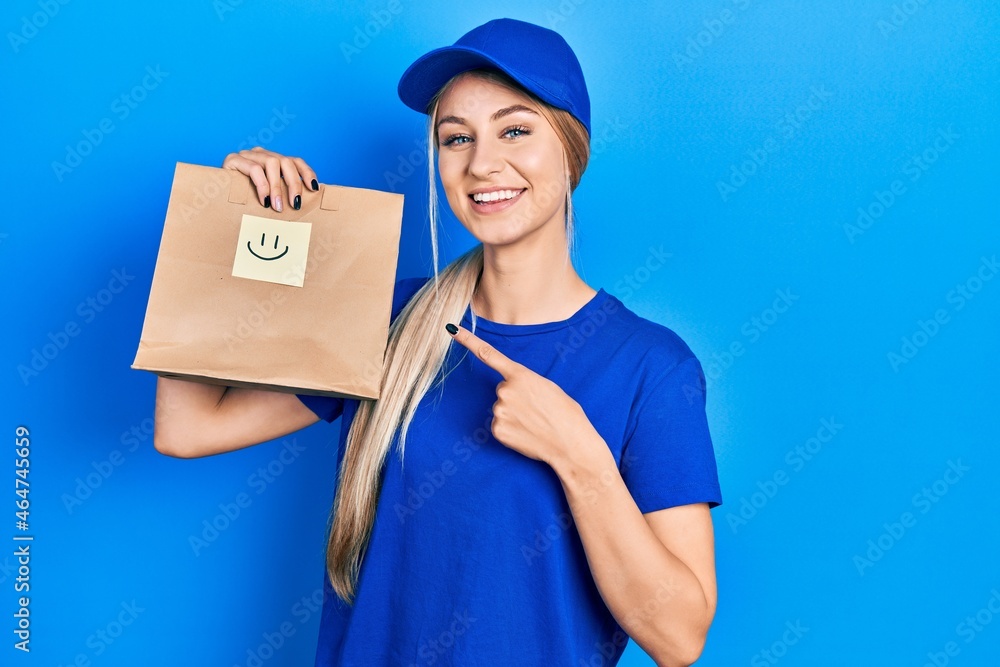 Young caucasian woman holding take away paper bag with happy face reminder smiling happy pointing with hand and finger Young caucasian woman holding take away paper bag with happy face reminder smiling happy pointing with hand and finger