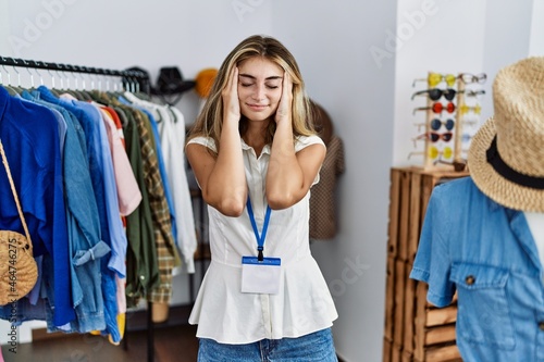 Young blonde woman working as manager at retail boutique with hand on head for pain in head because stress. suffering migraine.