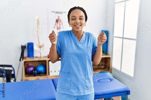Young african american woman working at pain recovery clinic excited for success with arms raised and eyes closed celebrating victory smiling. winner concept.