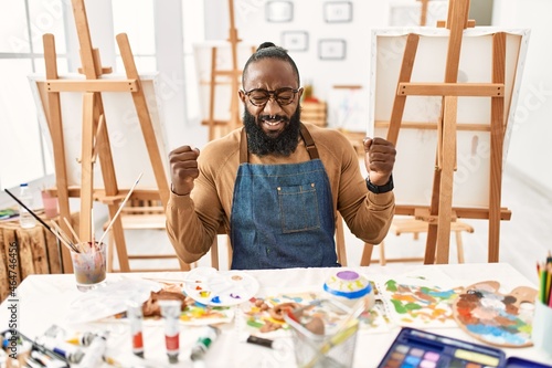 African american artist man at art studio excited for success with arms raised and eyes closed celebrating victory smiling. winner concept.