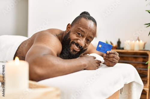 Young african american man smiling confident holding credit card at beauty center