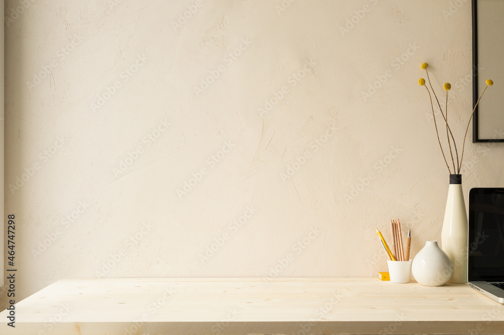 Home office desk with computer in the corner, design vase with dried flowers, cup with pencils, supplies against beige clay wall. Minimalist workspace.