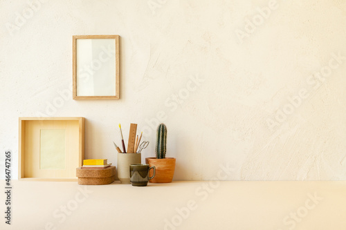 Table with art supplies, pencils, brushes cactus and drawing frame on beige clay textured wall with copy space. 