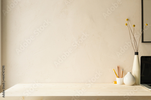 Fotografia Home office desk with computer in the corner, design vase with dried flowers, cup with pencils, supplies against beige clay wall