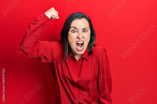 Middle age hispanic woman wearing casual clothes angry and mad raising fist frustrated and furious while shouting with anger. rage and aggressive concept. photo