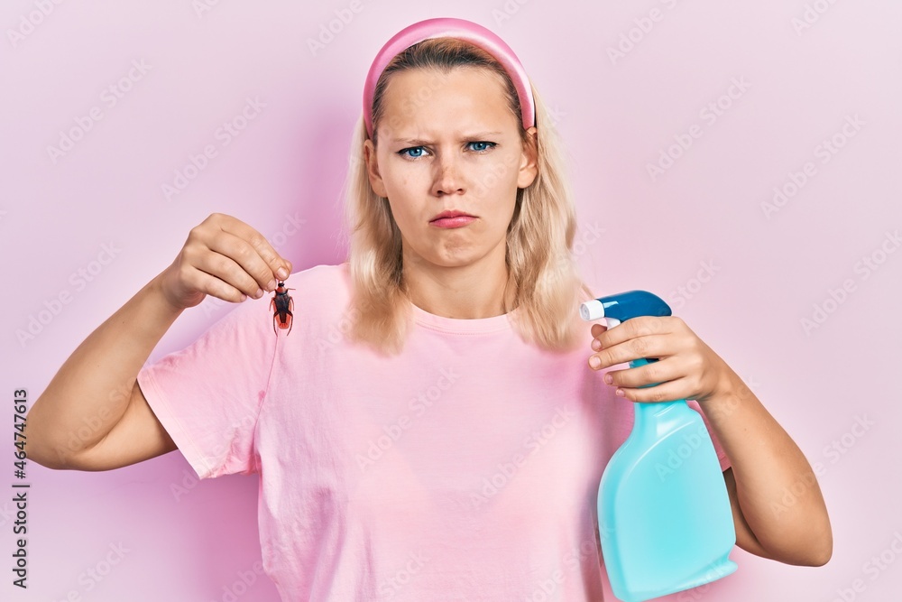 Beautiful caucasian blonde woman holding cockroach and pesticide sprayer depressed and worry for distress, crying angry and afraid. sad expression. Beautiful caucasian blonde woman holding cockroach and pesticide sprayer depressed and worry for distress, crying angry and afraid. sad expression.