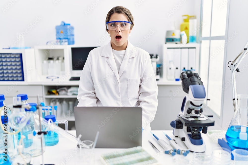 Young hispanic woman wearing scientist uniform working at laboratory scared and amazed with open mouth for surprise, disbelief face Young hispanic woman wearing scientist uniform working at laboratory scared and amazed with open mouth for surprise, disbelief face