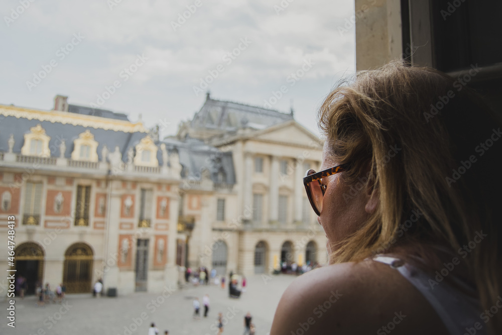 Mujer de perfil con gafas de sol marrones y un palacio de fondo de vacaciones contemplando las vistas.