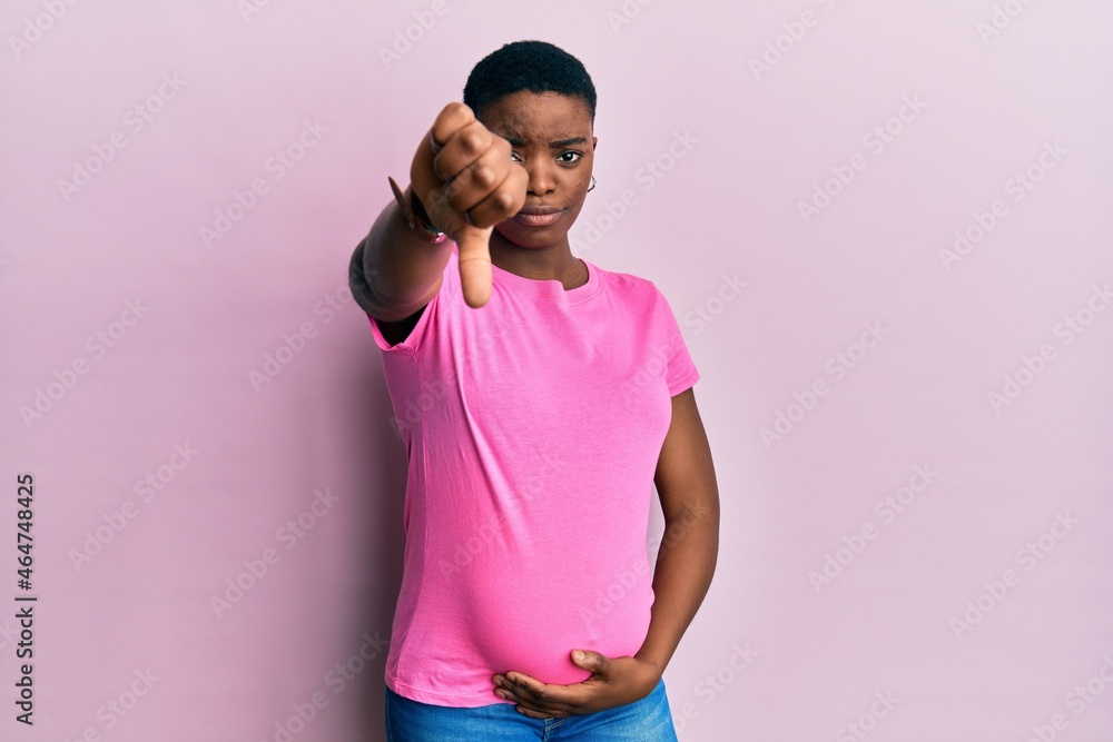 Young african american woman expecting a baby, touching pregnant belly looking unhappy and angry showing rejection and negative with thumbs down gesture. bad expression. Young african american woman expecting a baby, touching pregnant belly looking unhappy and angry showing rejection and negative with thumbs down gesture. bad expression.