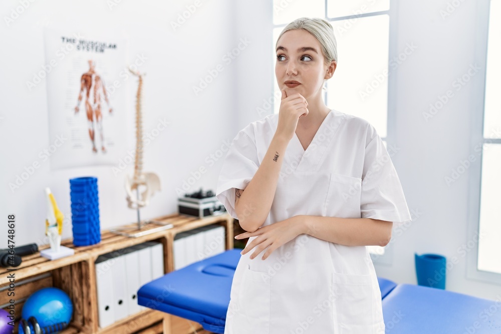 Young caucasian woman working at pain recovery clinic looking confident at the camera smiling with crossed arms and hand raised on chin. thinking positive. Young caucasian woman working at pain recovery clinic looking confident at the camera smiling with crossed arms and hand raised on chin. thinking positive.