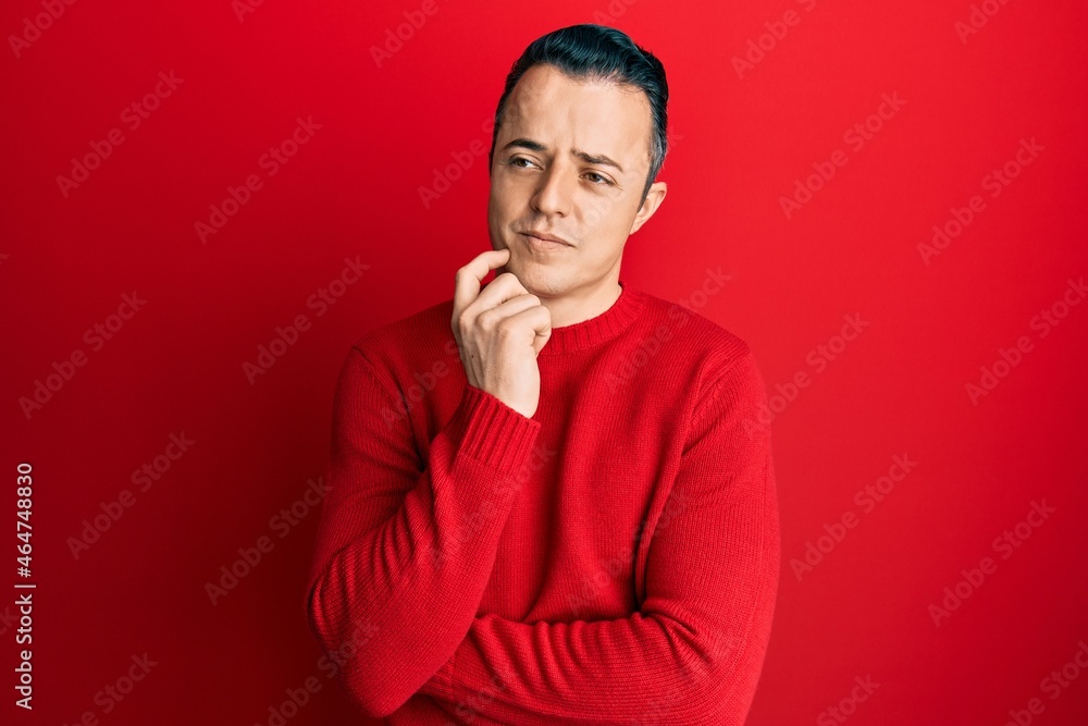 Handsome young man wearing casual winter sweater thinking concentrated about doubt with finger on chin and looking up wondering Handsome young man wearing casual winter sweater thinking concentrated about doubt with finger on chin and looking up wondering
