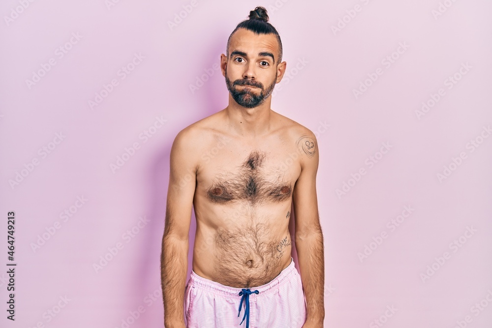 Fototapeta premium Young hispanic man shirtless wearing swimsuit puffing cheeks with funny face. mouth inflated with air, crazy expression.