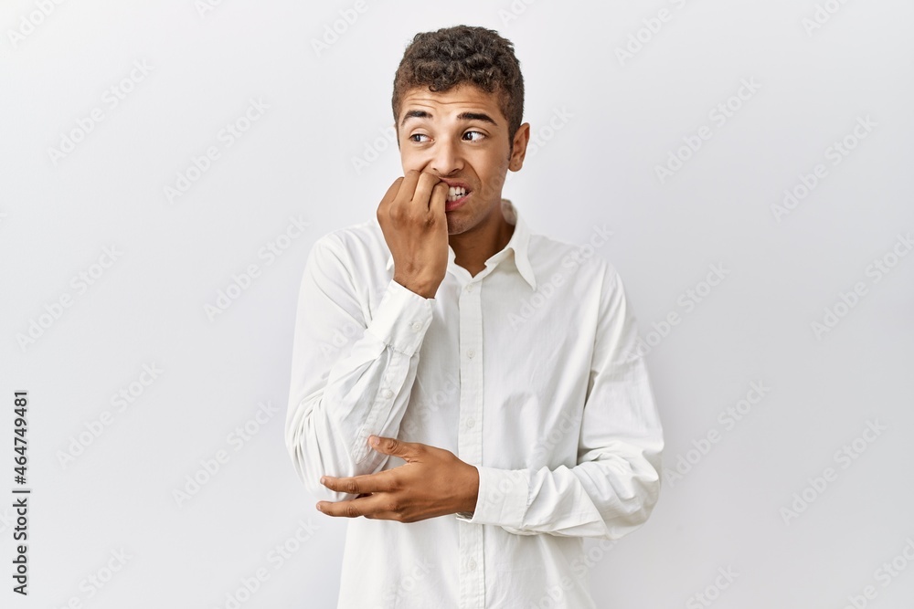 Young handsome hispanic man standing over isolated background looking stressed and nervous with hands on mouth biting nails. anxiety problem. Young handsome hispanic man standing over isolated background looking stressed and nervous with hands on mouth biting nails. anxiety problem.