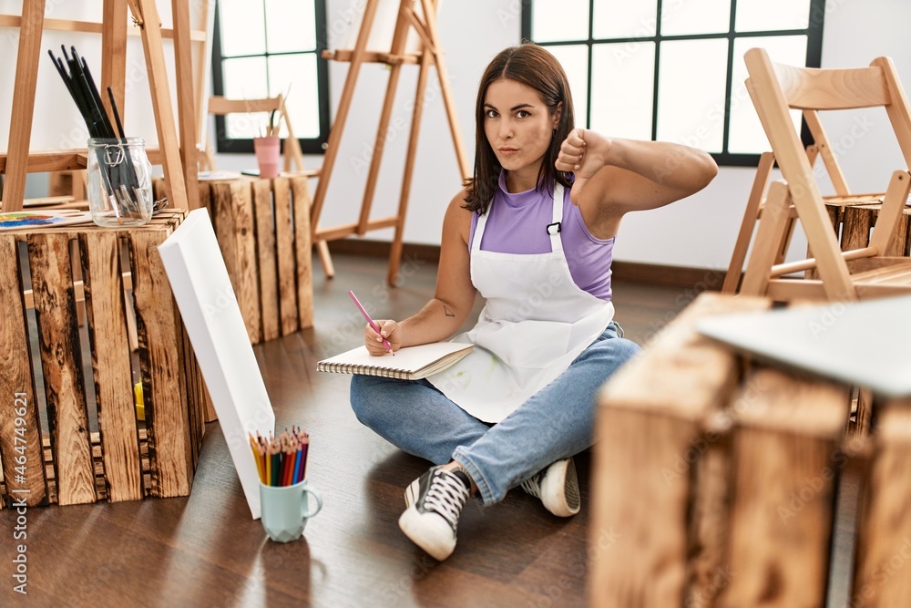 Young beautiful hispanic woman at art studio with angry face, negative sign showing dislike with thumbs down, rejection concept