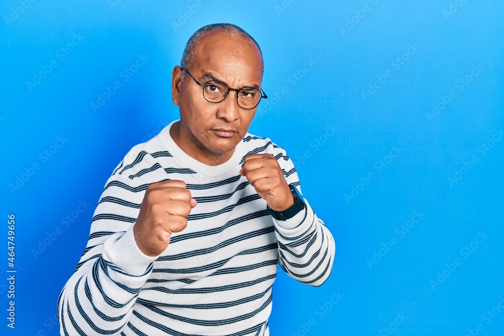 Middle age latin man wearing casual clothes and glasses ready to fight with fist defense gesture, angry and upset face, afraid of problem Middle age latin man wearing casual clothes and glasses ready to fight with fist defense gesture, angry and upset face, afraid of problem