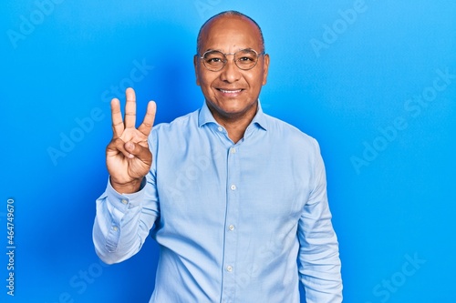 Middle age latin man wearing casual clothes and glasses showing and pointing up with fingers number three while smiling confident and happy. © Krakenimages.com