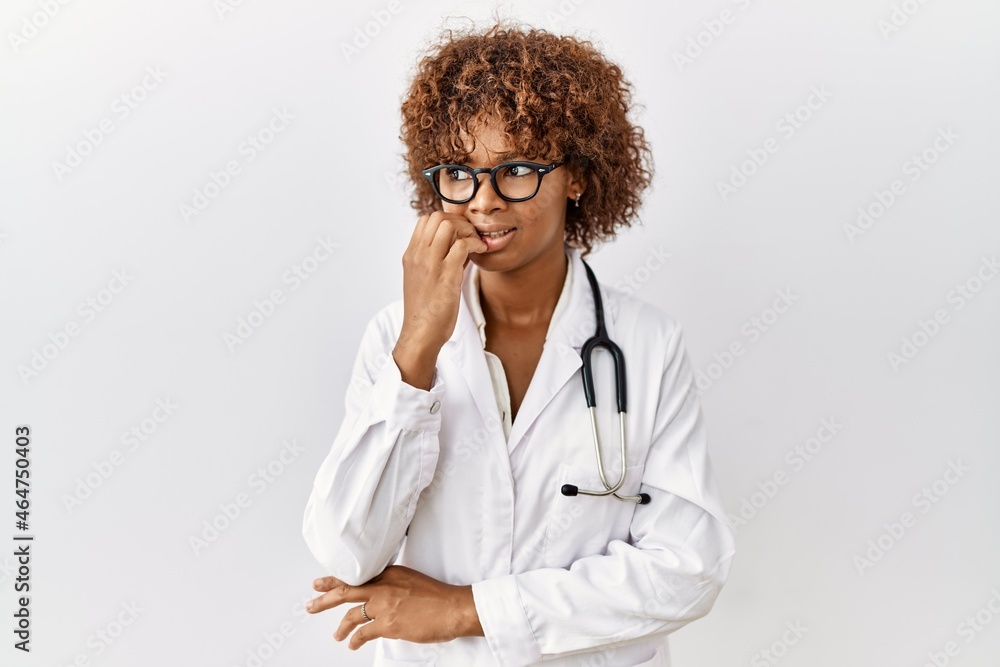 Young african american woman wearing doctor uniform and stethoscope looking stressed and nervous with hands on mouth biting nails. anxiety problem.