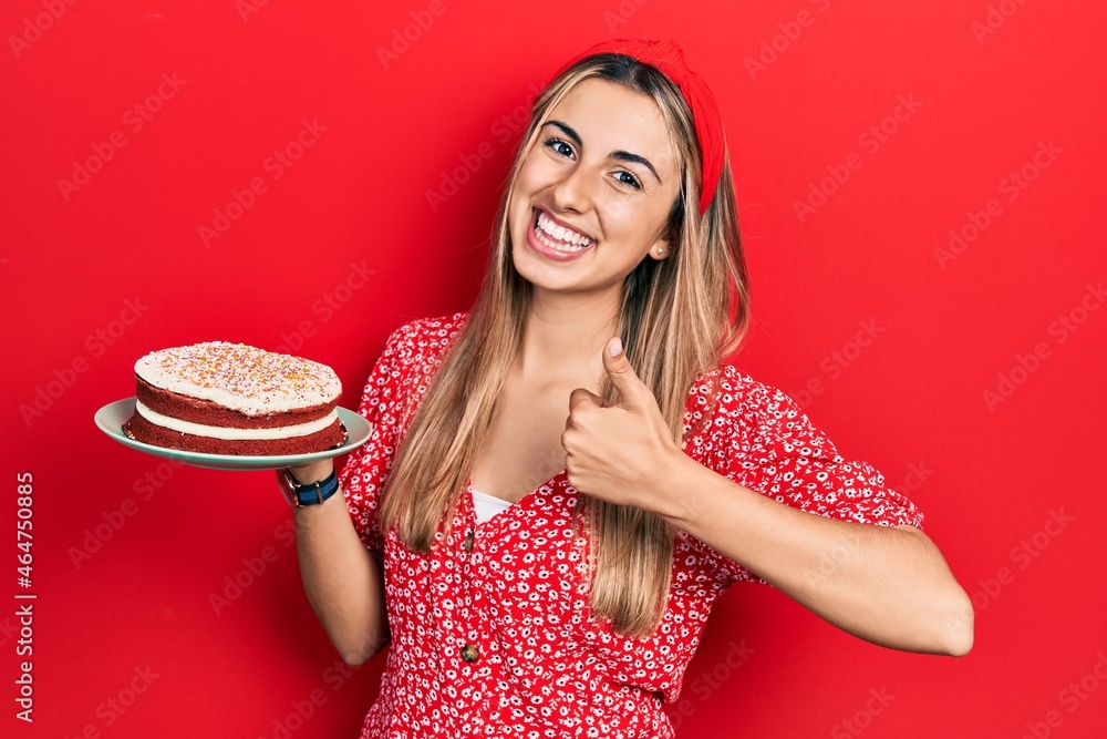 Beautiful hispanic woman holding strawberry cake smiling happy and positive, thumb up doing excellent and approval sign Beautiful hispanic woman holding strawberry cake smiling happy and positive, thumb up doing excellent and approval sign